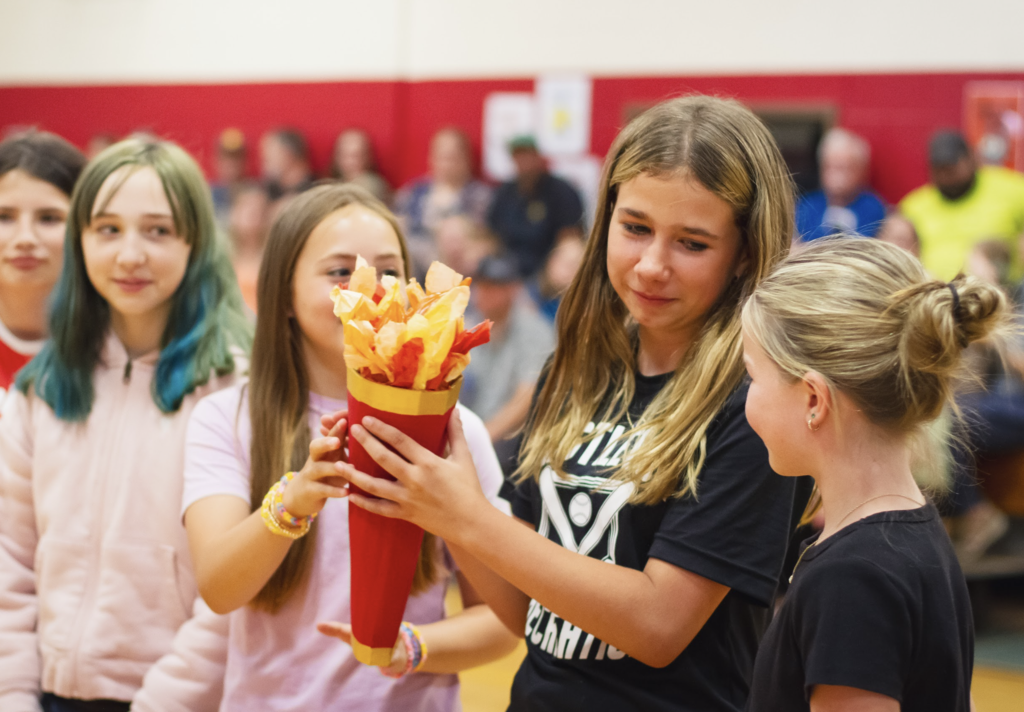 A group of students participates in the symbolic passing of the torch, holding a handmade torch decorated with red, orange, and yellow tissue paper flames.