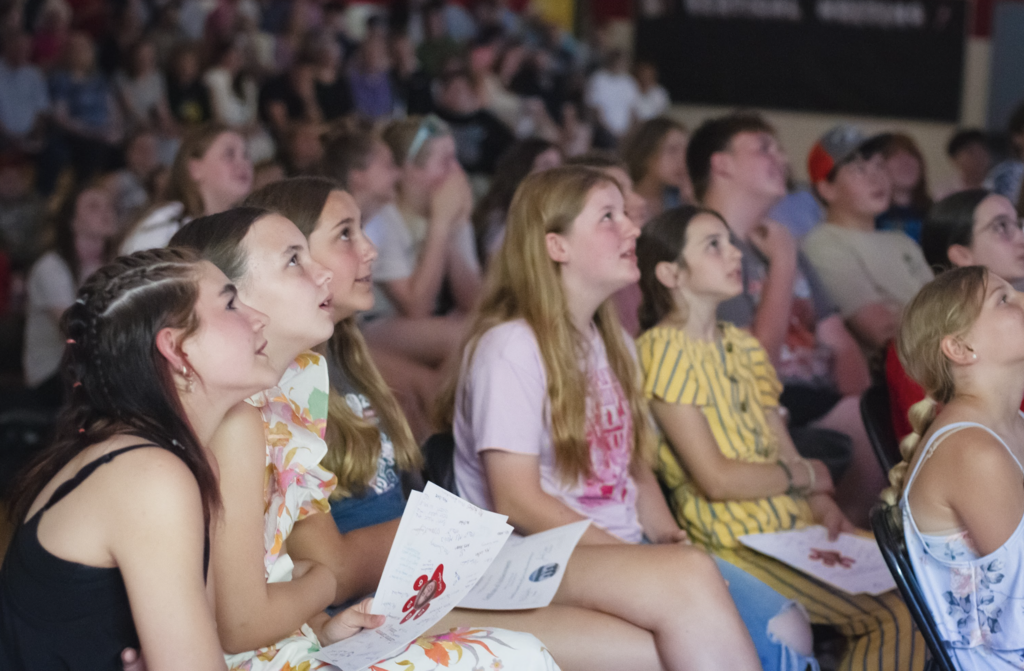 Sixth-grade students laugh and smile while watching a slideshow featuring baby photos and memories from their elementary school years.