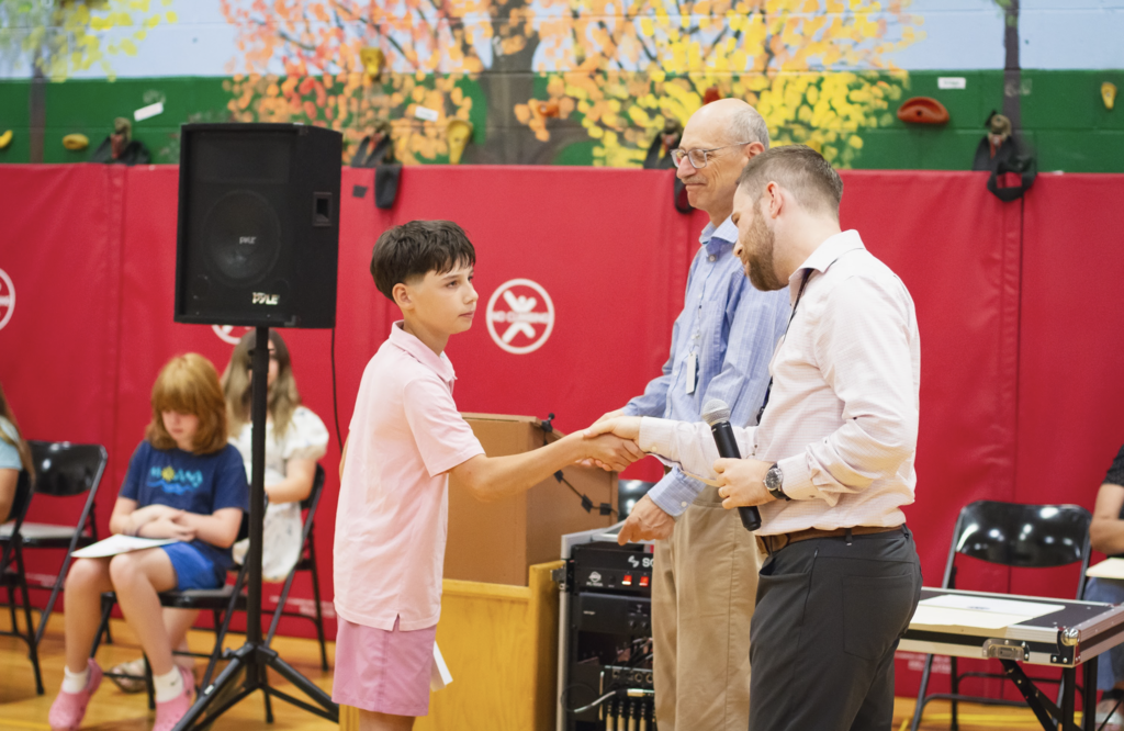 A sixth-grade student shakes hands with Principal Danyow after receiving recognition during the Torch Ceremony.