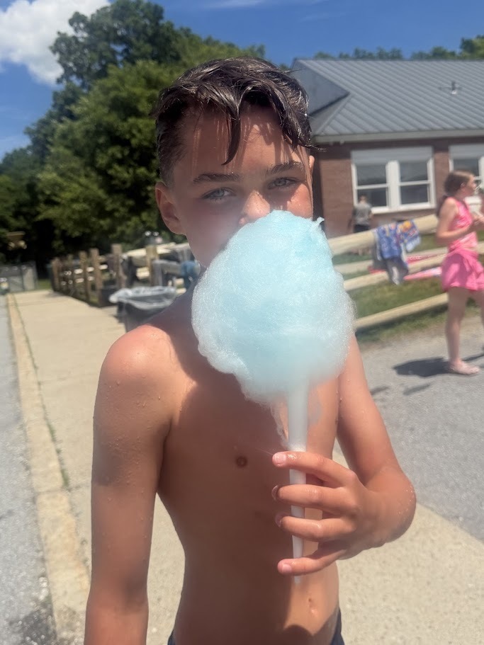 A student holds a large blue cotton candy while standing outside on a sunny day during school field day activities.