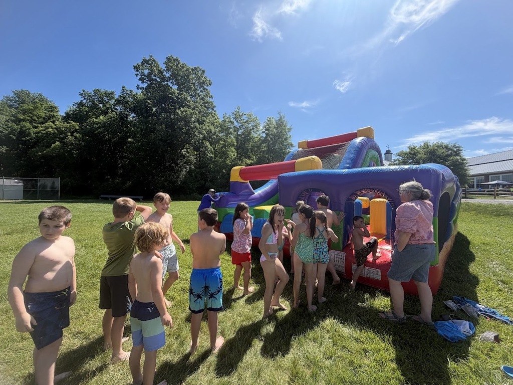 Students gather around a colorful inflatable obstacle course, waiting their turn to climb, crawl, and slide during outdoor field day festivities.
