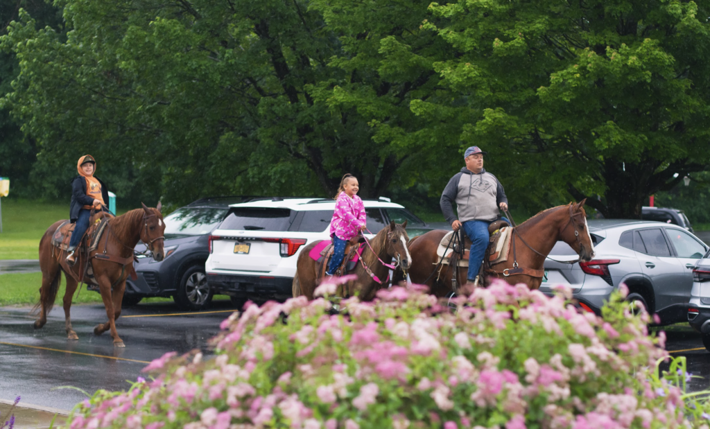 Two students and a parent ride horses through the school parking lot while arriving for the last day of school.