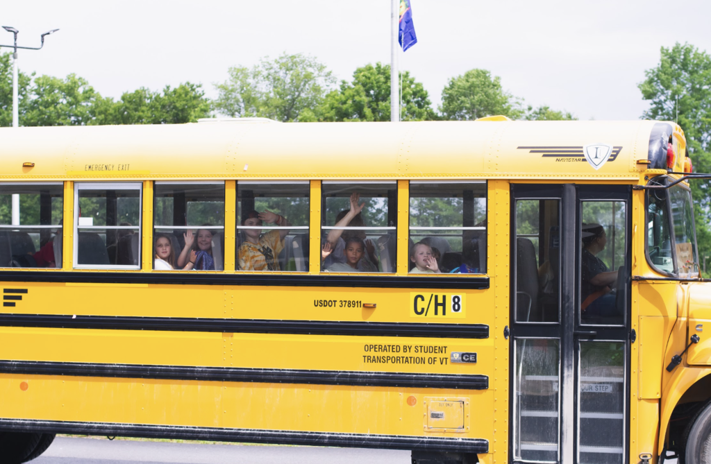Students wave from the windows of a school bus as it departs on the final day of school.