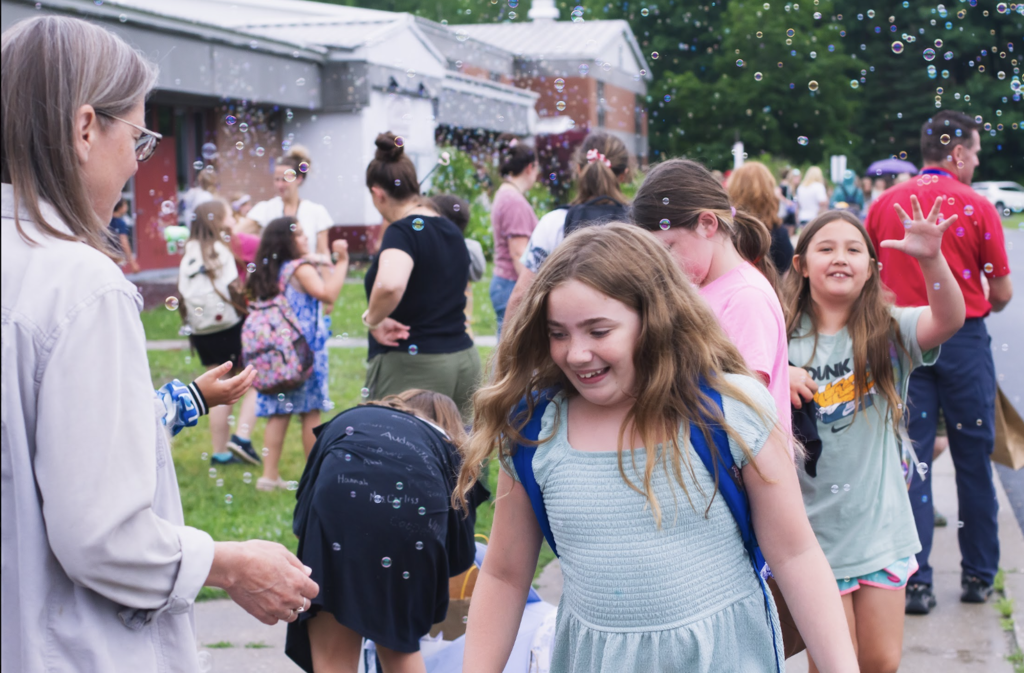 Students and families walk through floating bubbles outside the school entrance during last-day celebrations.