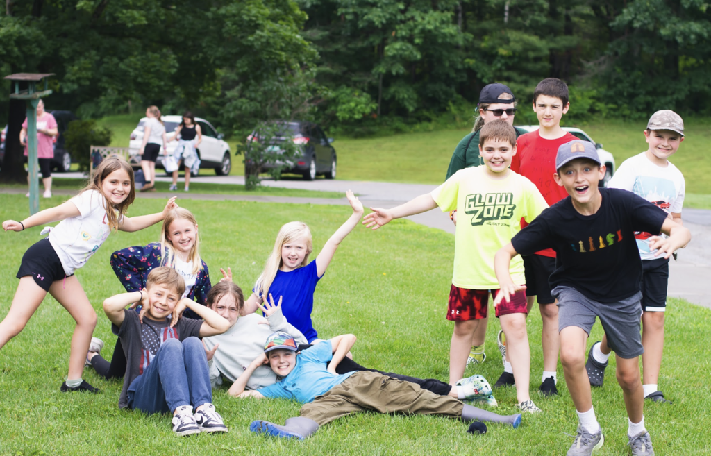 A group of elementary students pose playfully on the grass, smiling and making silly gestures for the camera.