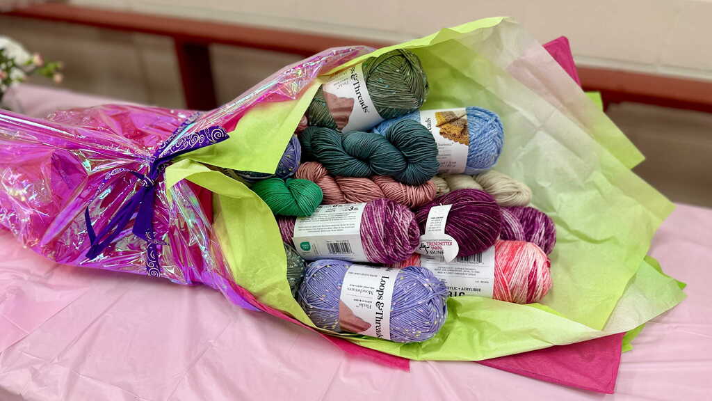 A large bouquet made from colorful skeins of yarn, knitting supplies, and tissue paper sits on a table as a retirement gift honoring librarian Tina Rampone's love of knitting.