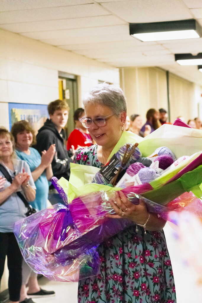 Tina Rampone carries a large bouquet made of yarn and knitting supplies as colleagues line the hallway applauding and celebrating her retirement.