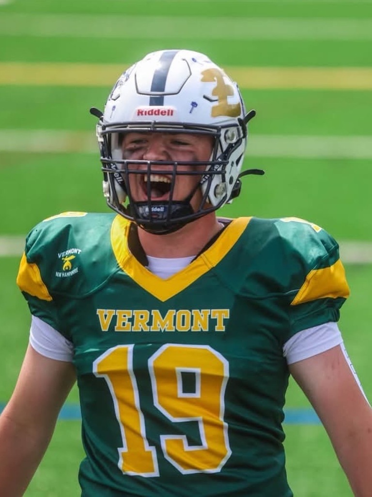 A football player wearing a green and gold Vermont jersey with number 19 and a white helmet celebrates on the field with his mouth open in excitement during the 73rd Maple Sugar Bowl.