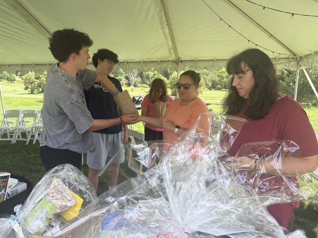 Students and adults work together under a tent preparing and organizing items during the Senior Class Golf Fundraiser, highlighting the volunteers who helped make the event possible.