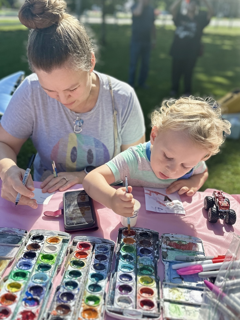 A young child and an adult create miniature artwork together using watercolor paints at the community art table.