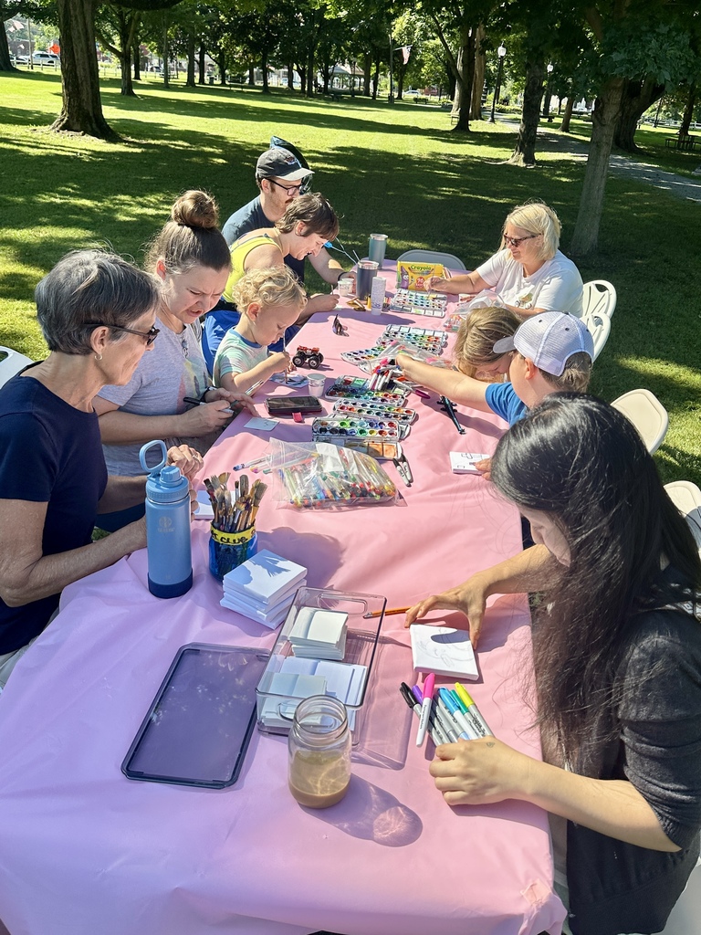 Children and adults gather around a table in Fair Haven Park, using paints, markers, and other supplies to create miniature artwork.