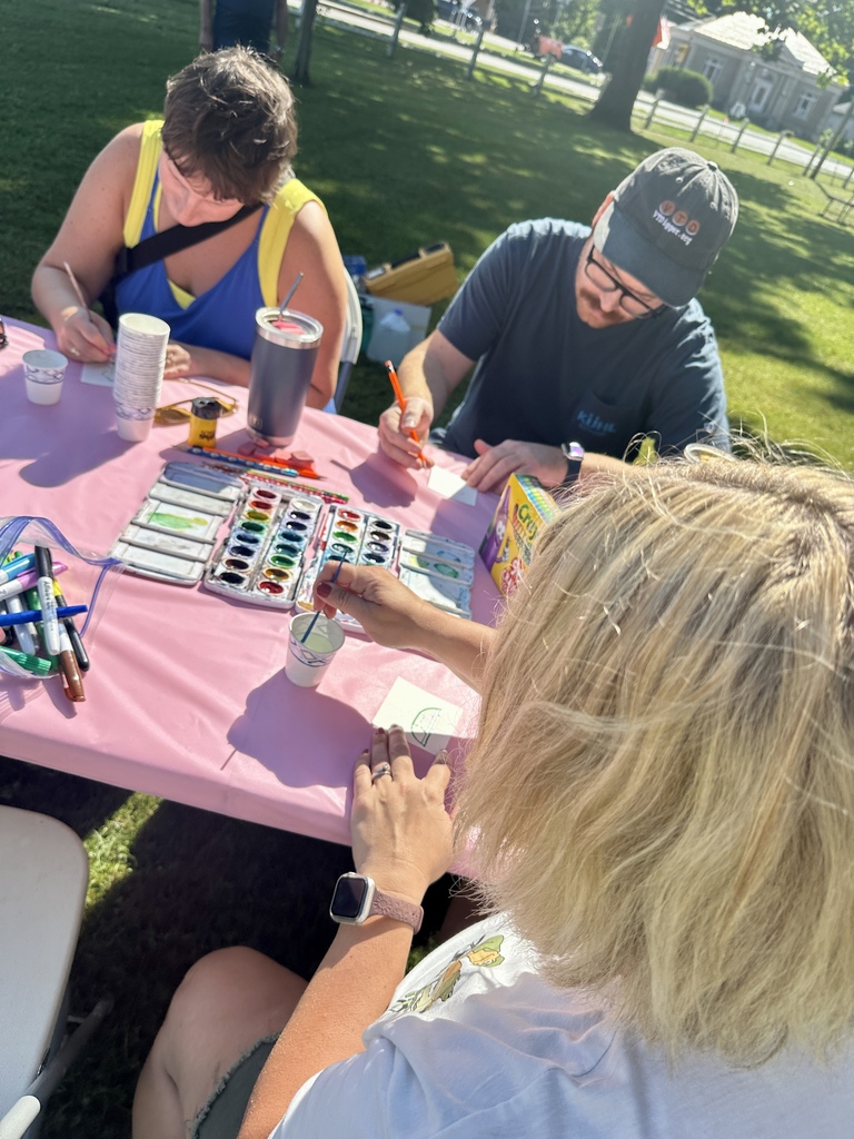 Community members sit around an outdoor table creating small works of art with watercolor paints and other supplies in Fair Haven Park.