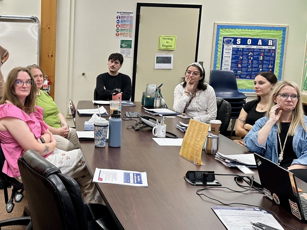 New Slate Valley educators sit around a conference table during New Teacher Orientation, listening to a presentation and reviewing materials.