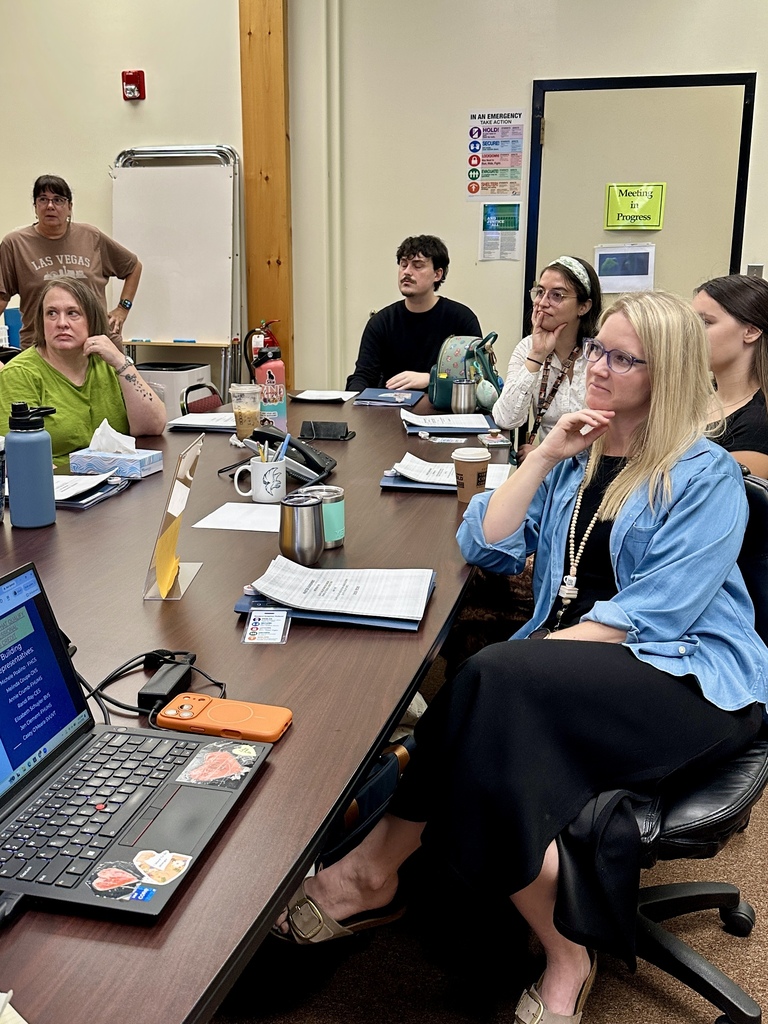 New Slate Valley staff members gather around a conference table during orientation, listening attentively to information being shared as they prepare for the new school year.