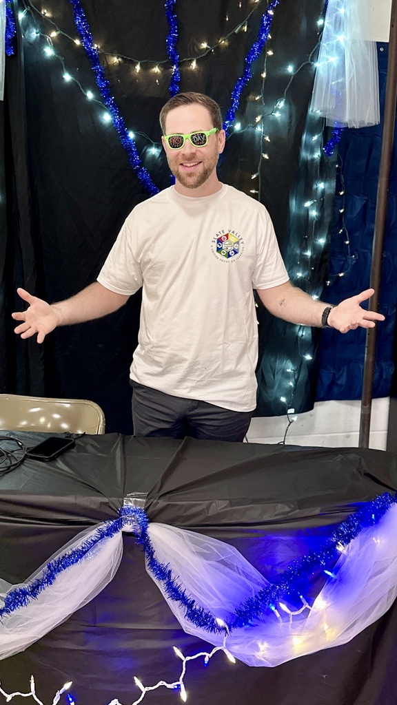 A Slate Valley staff member wearing “First Day 2026” glasses poses behind the decorated Opening Day DJ booth.