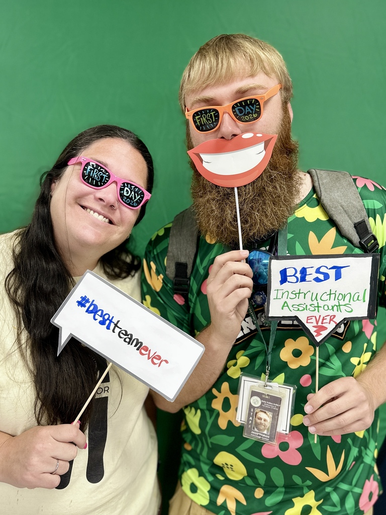 Two Slate Valley staff members pose at the Opening Day photo booth wearing colorful “First Day 2026” glasses and holding team-themed props.