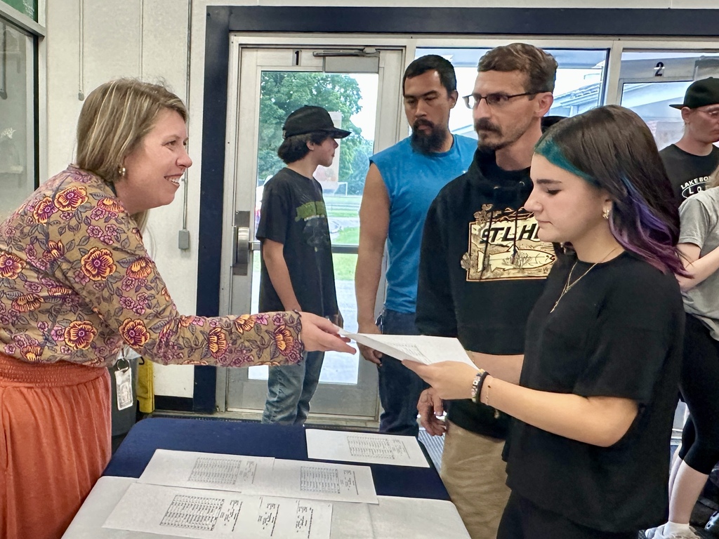 A staff member hands a schedule to a family as students and parents check in during Middle School Open House.