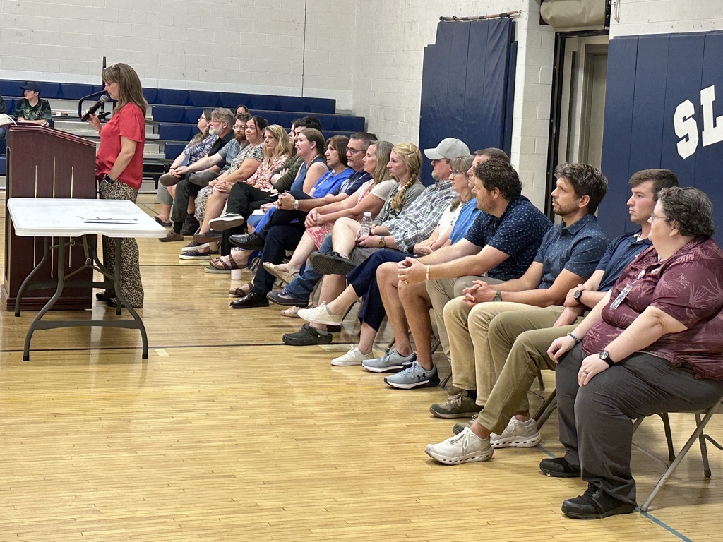 Principal Jennefer Paquette speaks at a podium while middle school faculty and staff sit nearby during Open House.