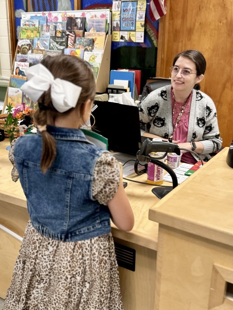 A CES student with a large white bow talks with a staff member at the library desk during Open House.