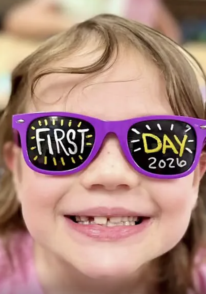 Close-up of a smiling student wearing bright purple sunglasses decorated with the words “First Day 2026” on the lenses.