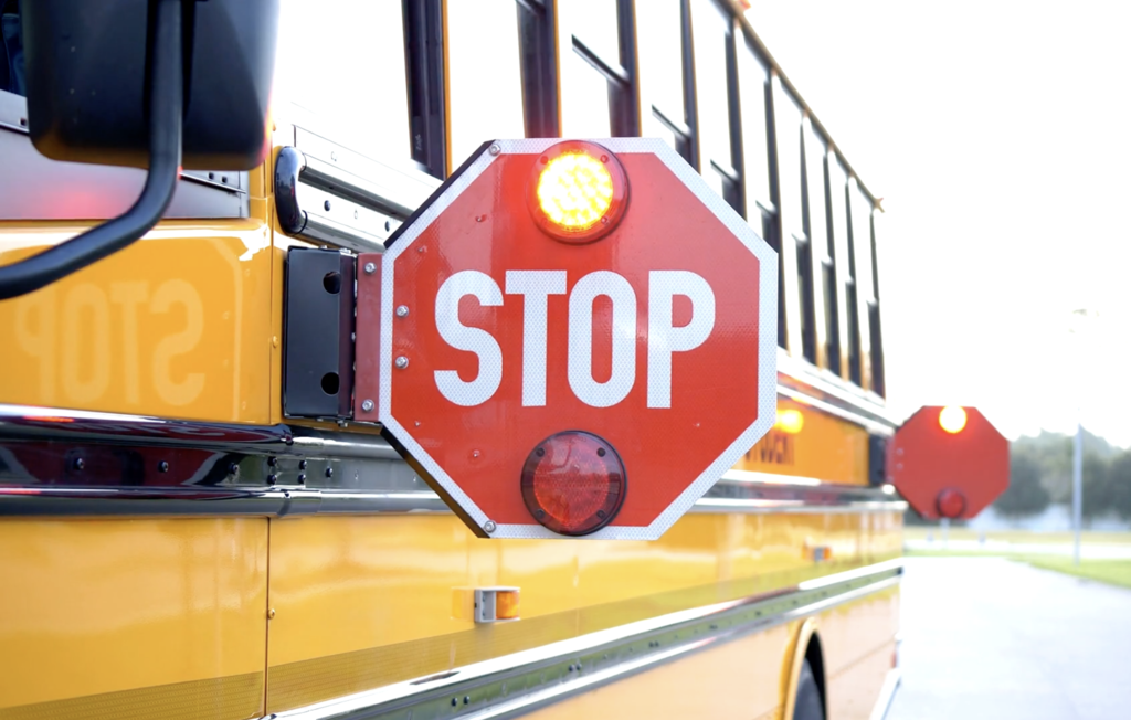 Animated image of a yellow school bus with its red stop arm extended and red warning lights flashing, reminding drivers to stop when students are getting on or off the bus.