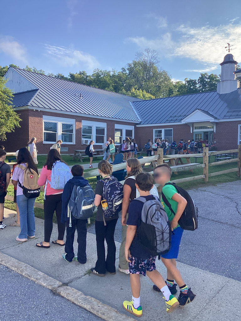 Students wearing backpacks gather outside the school building and make their way toward the entrance on the first day of school.