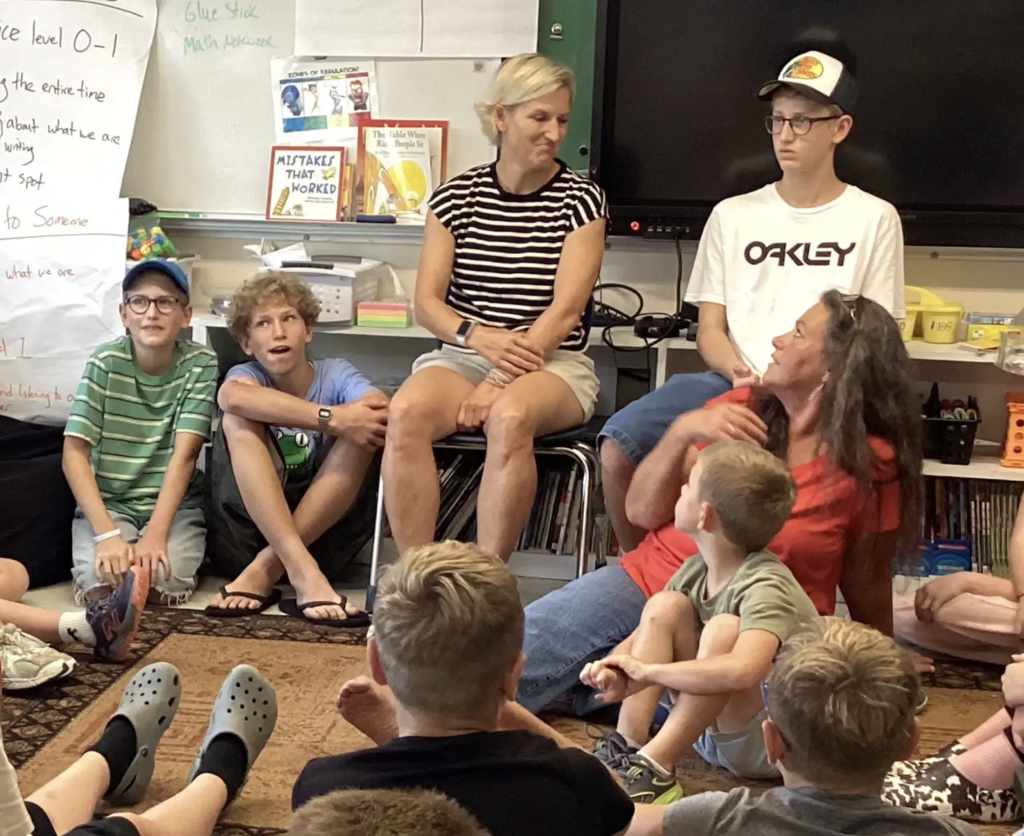 Closer view of students and adults seated together during a classroom discussion, with several participants listening as one adult speaks to the group.