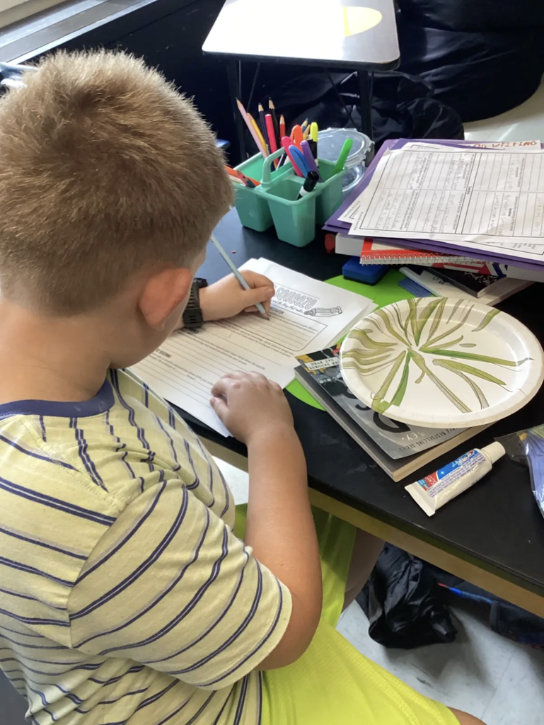 Student writes observations on “The Big Squeeze” science worksheet after examining a toothpaste sample during a classroom investigation.
