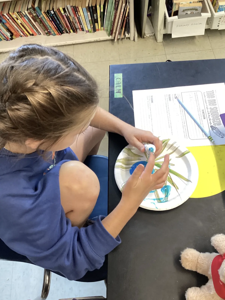 Student uses a tube to squeeze blue toothpaste onto a paper plate while completing “The Big Squeeze” science investigation worksheet.