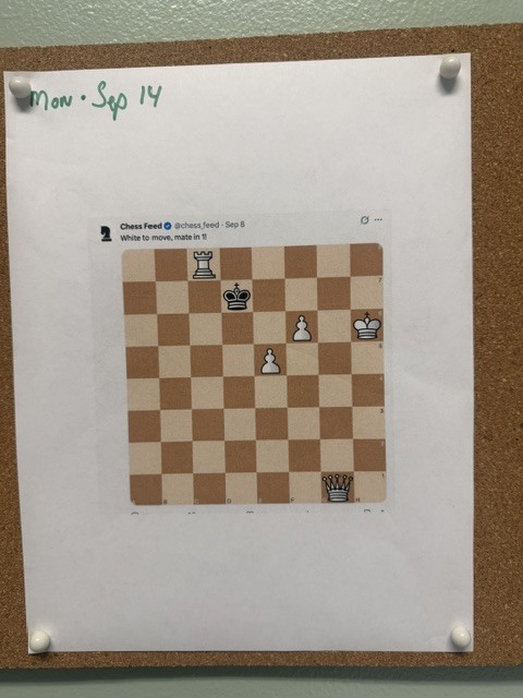 Close-up of the weekly OVS Chess Challenge posted on a corkboard, showing a chessboard puzzle with the prompt, “White to move, mate in 1.”