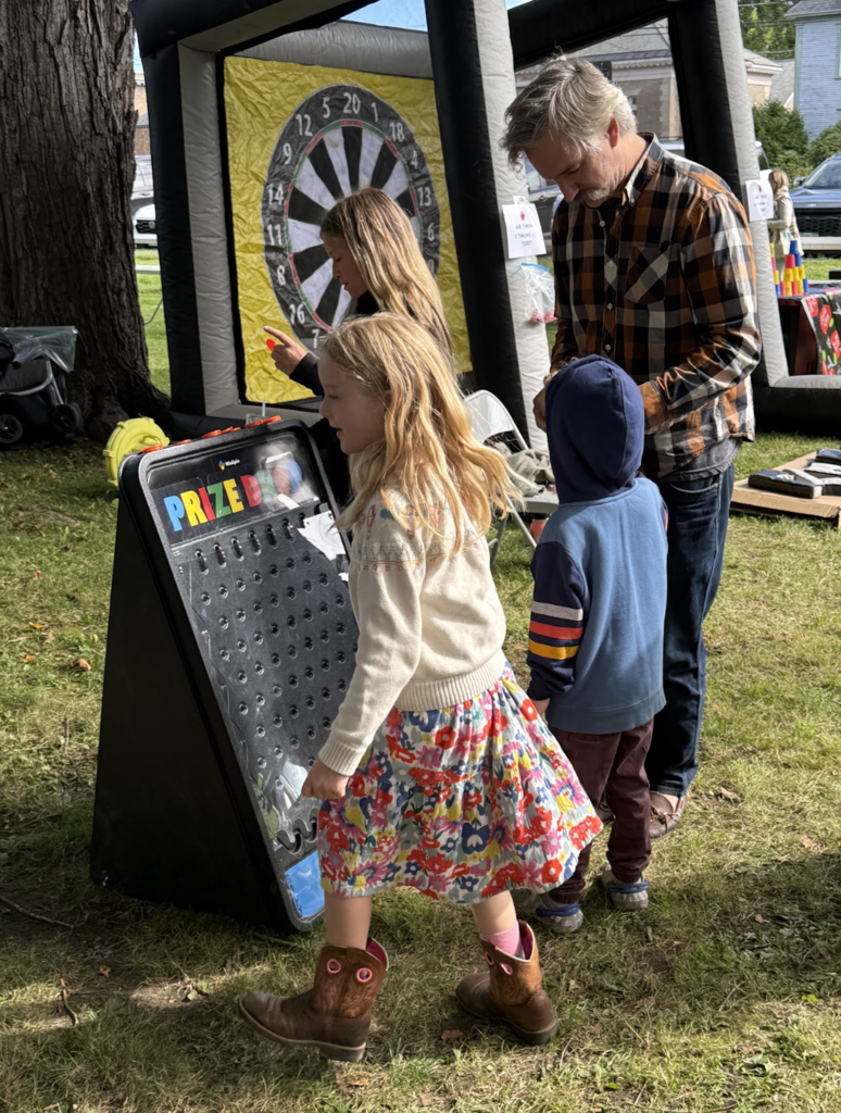 A young girl plays a tall Plinko-style prize game in front of an inflatable dart board activity.