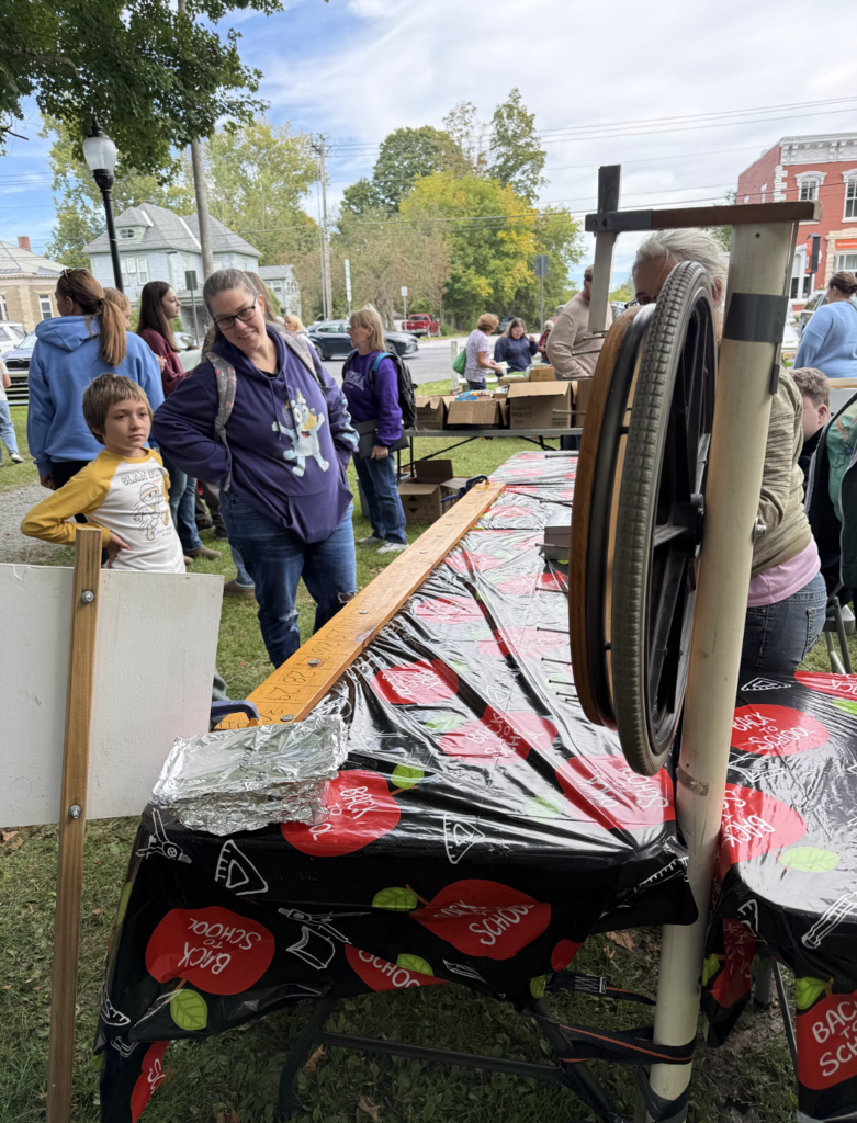 A young boy and a woman stand behind a long table set up for a cake wheel game at the park.