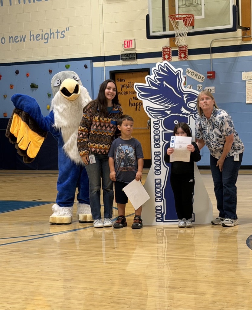Two students holding award certificates stand between two staff members and the falcon mascot during the ceremony.