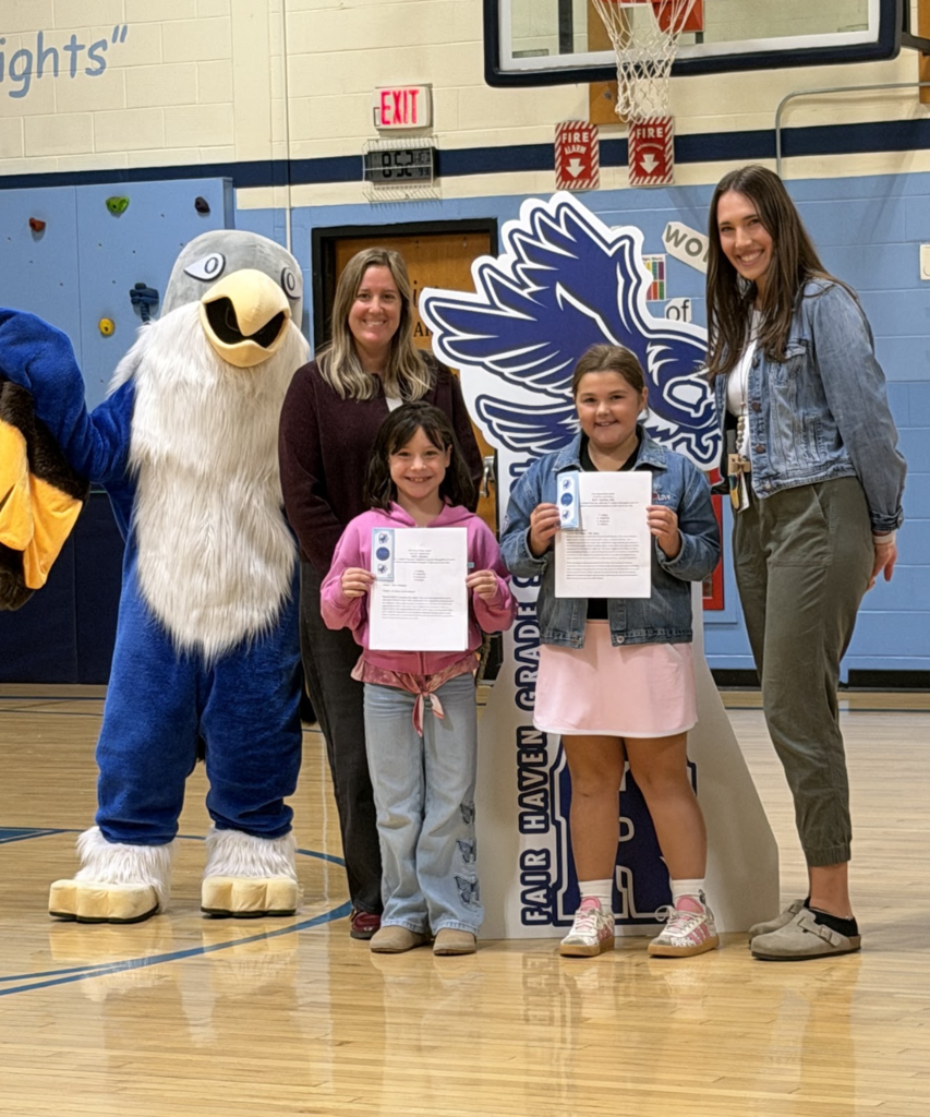 Two students proudly hold their award papers alongside two staff members and the falcon mascot.