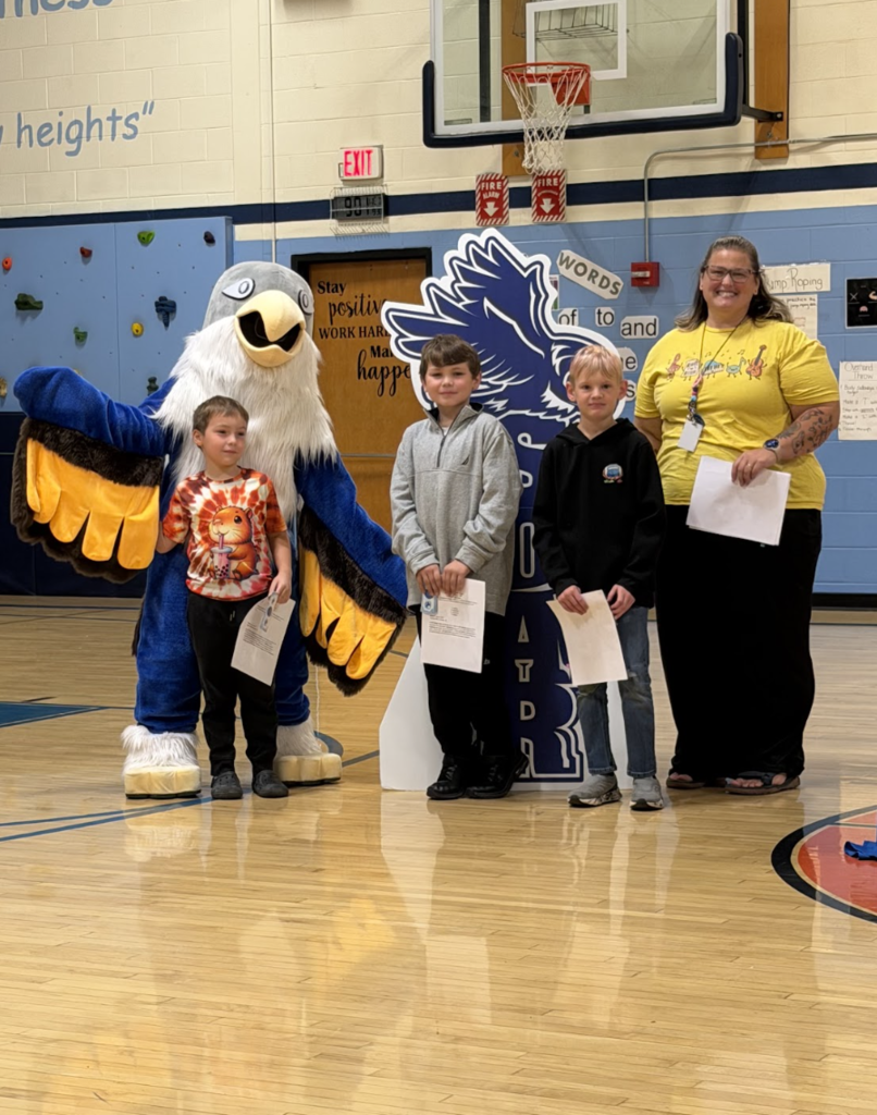 Three students holding award certificates stand with an adult staff member and the falcon mascot during the event.