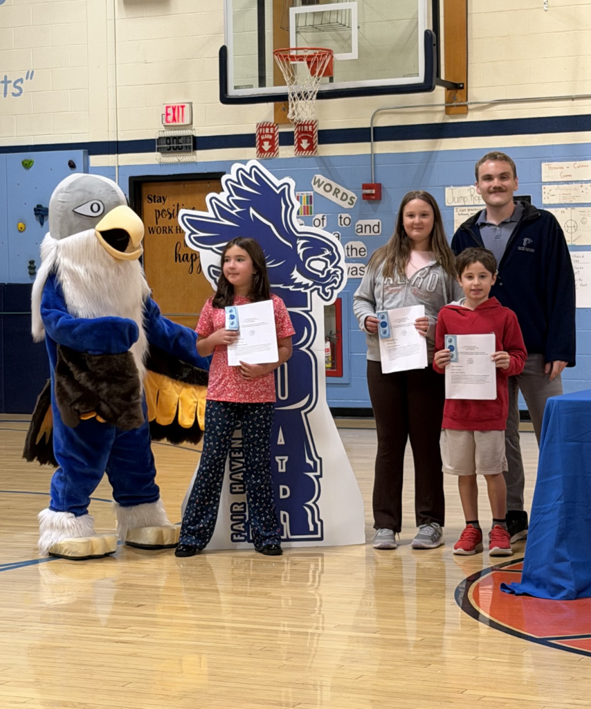 Three students holding award certificates stand with an adult staff member and the falcon mascot during the event.