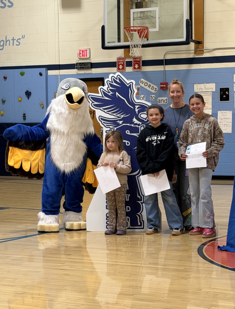 Three students holding award certificates stand with an adult staff member and the falcon mascot during the event.