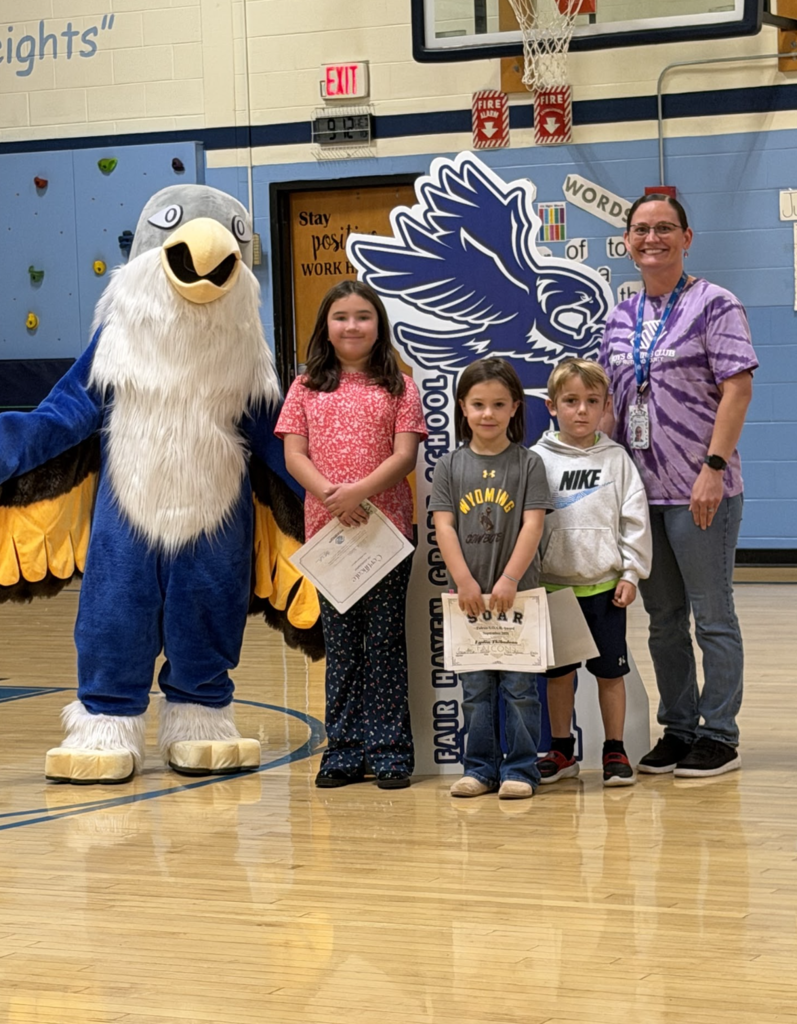 Three students holding award certificates stand with an adult staff member and the falcon mascot during the event.