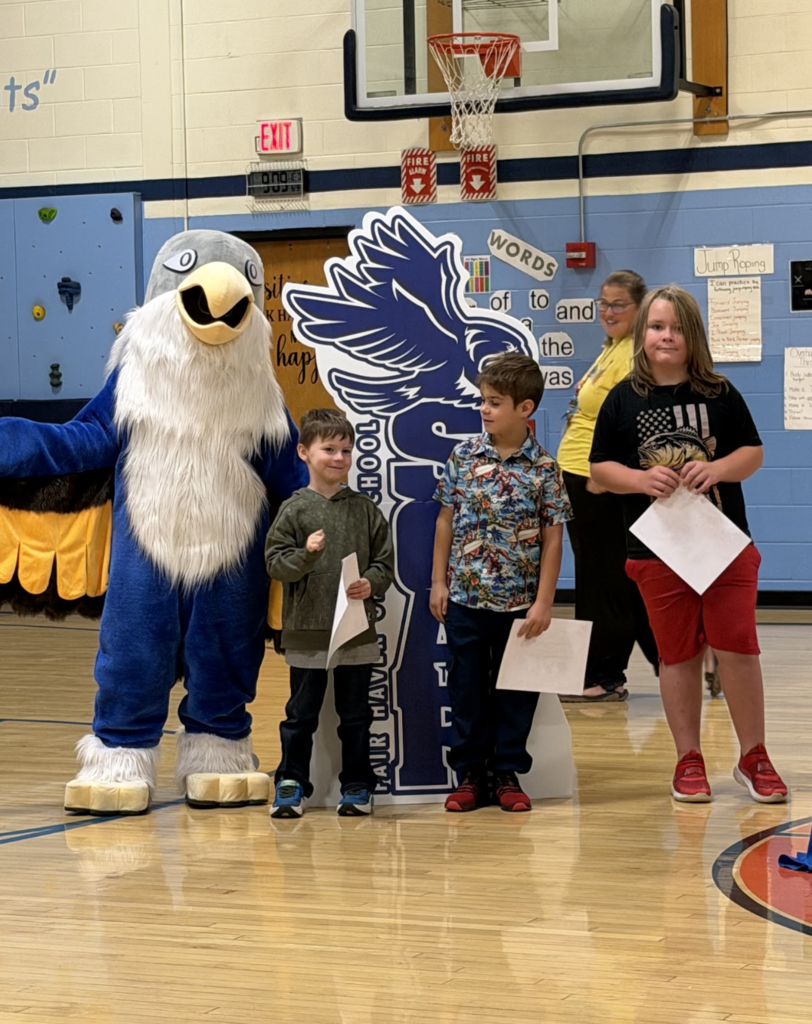 Three students holding award certificates stand with an adult staff member and the falcon mascot during the event.