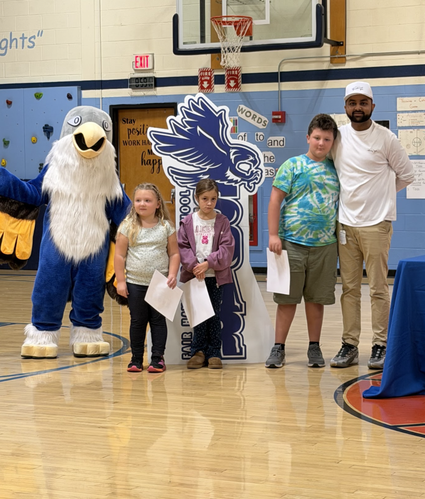 Three students holding award certificates stand with an adult staff member and the falcon mascot during the event.