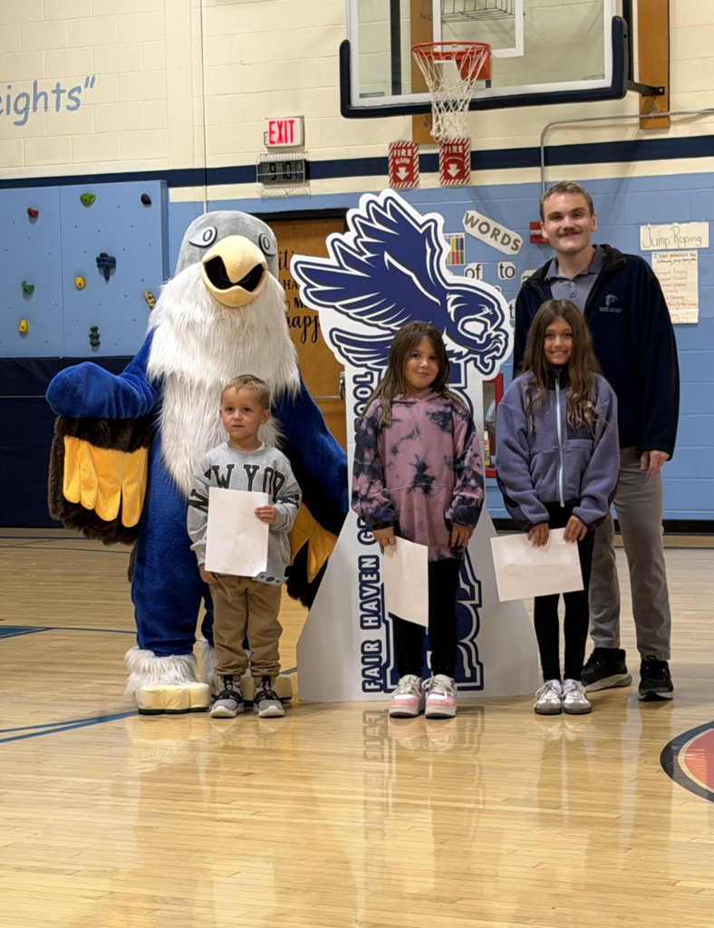 Three students holding award certificates stand with an adult staff member and the falcon mascot during the event.