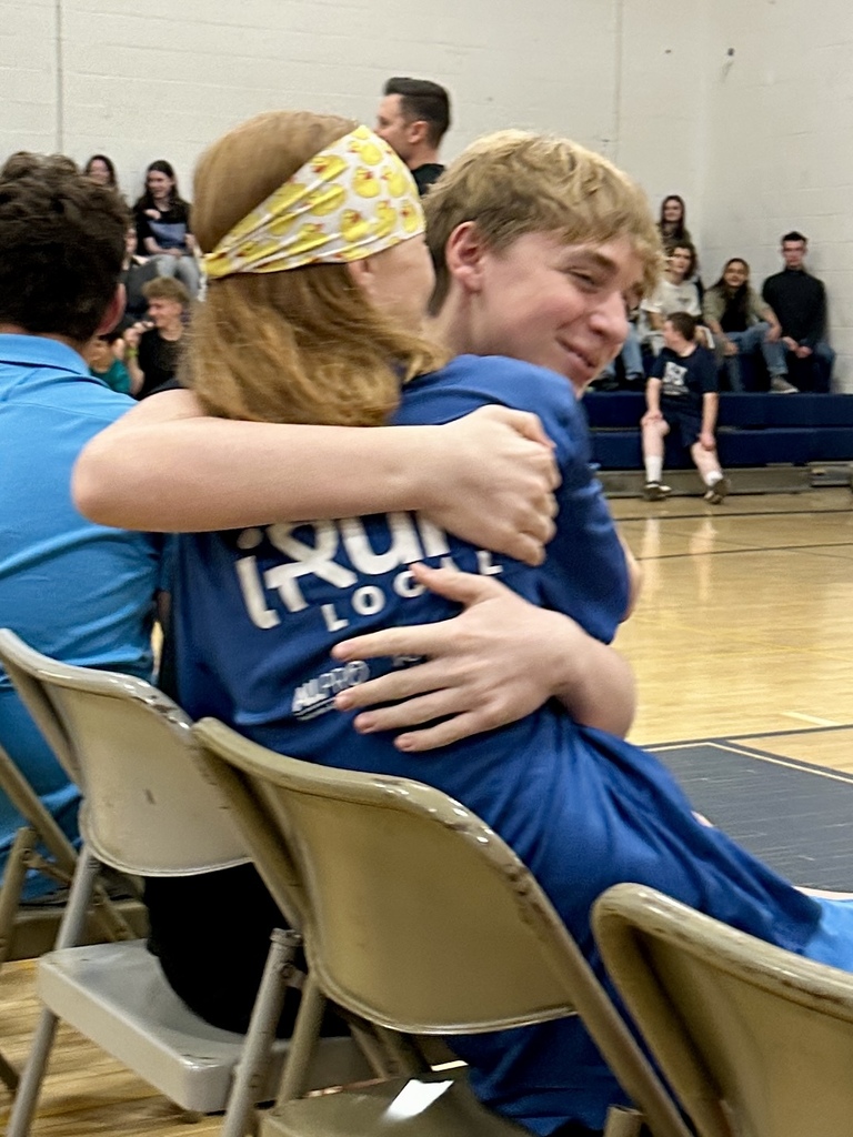 Two students sharing a warm hug on folding chairs during the school presentation.