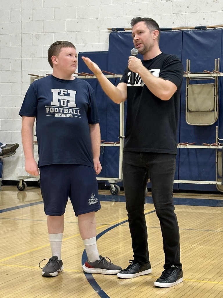 Speaker Brandon Lee White gesturing while interacting with a student on stage wearing an FHU Football shirt.