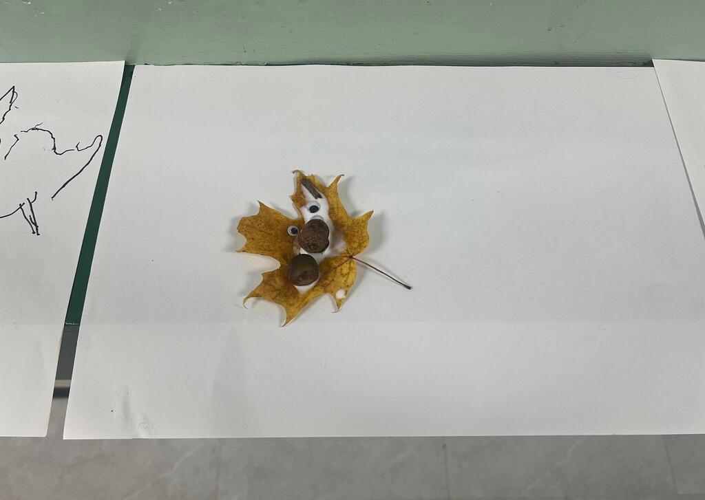 Student artwork featuring a single yellow leaf with googly eyes, small twigs, and acorns stuck with white glue.
