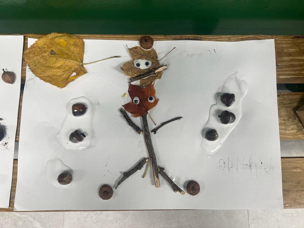 Student artwork showing a central stick-and-leaf figure surrounded by acorns glued on white paper.