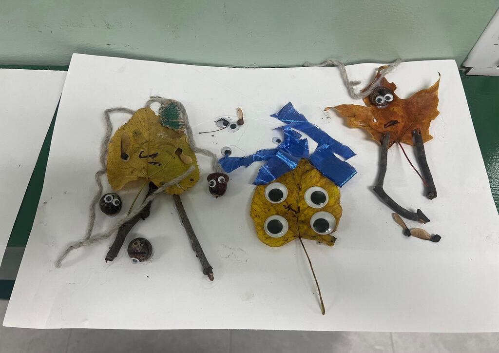 Student artwork displaying three leaf-and-stick figures decorated with googly eyes, yarn, and blue ribbon.