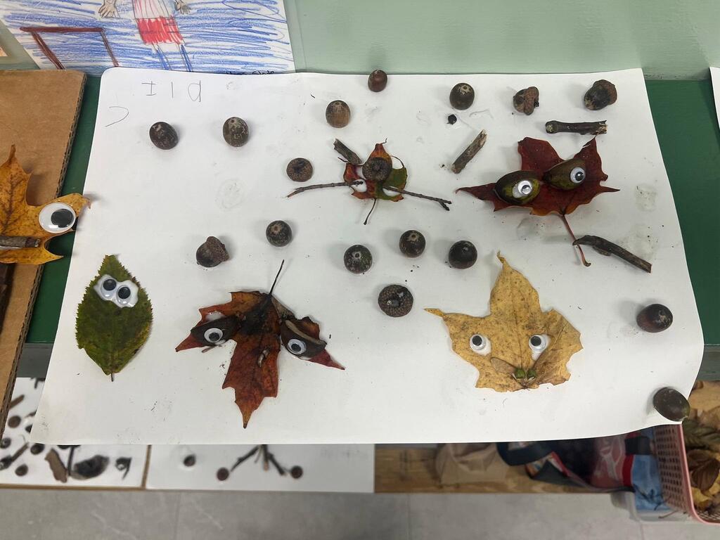 Student artwork titled "Eli," featuring multiple leaf creatures with googly eyes scattered among scattered acorns.