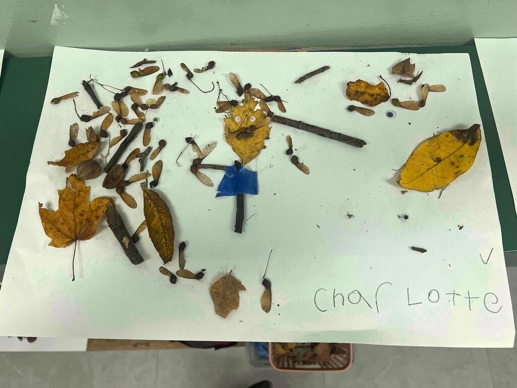 Student artwork by Charlotte featuring a stick-and-leaf figure with googly eyes surrounded by maple seed pods.