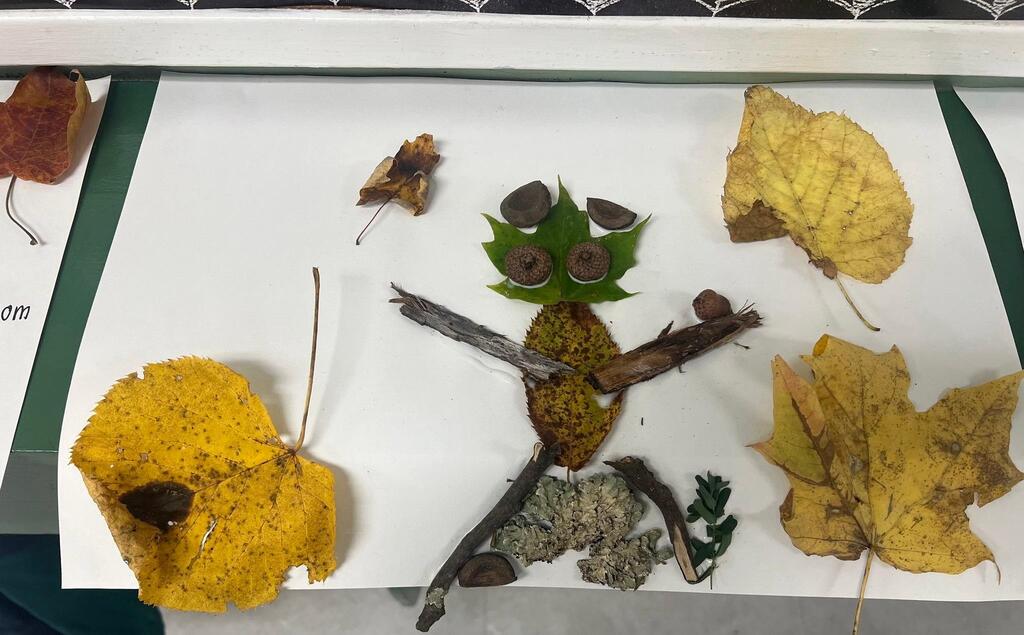 Student artwork of a figure crafted from sticks, leaves, acorns, and lichen on white paper.
