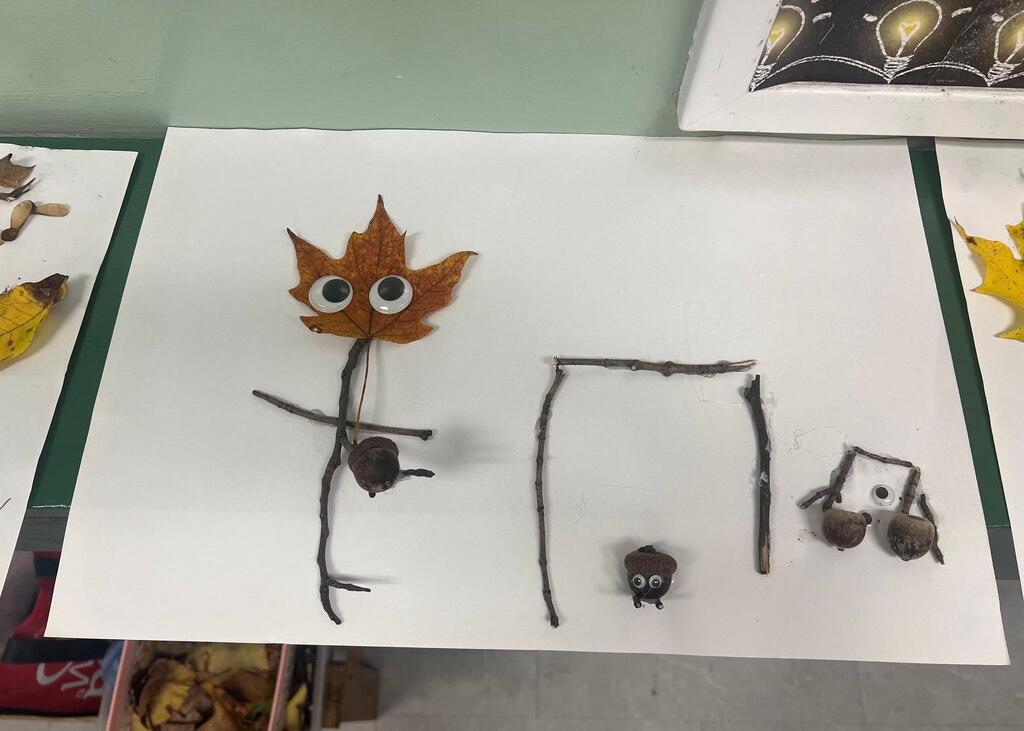 Student artwork depicting figures made from a leaf with googly eyes and stick structures glued onto paper.